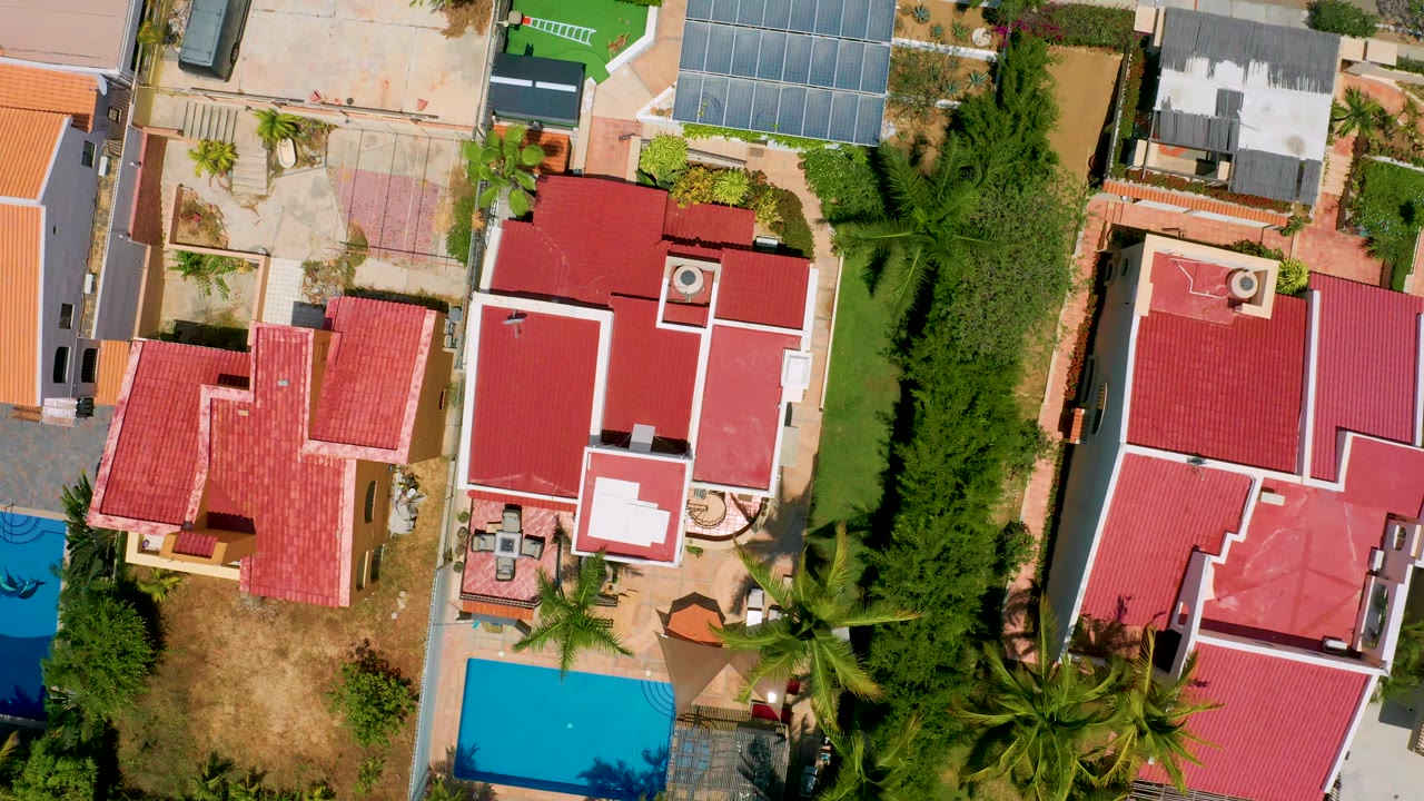 San Jose del Cabo aerial frame showing clustered red-roof houses, a turquoise pool edge, pale pavement, garden plantings, and no visible people.