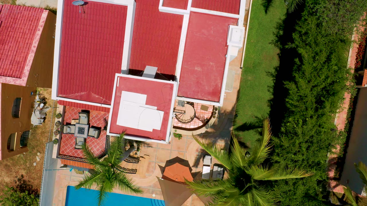 Overhead San Jose Del Cabo view with the red roof and white roof panel centered, patio furniture near the lower left, hedges along the right side, and no visible people.