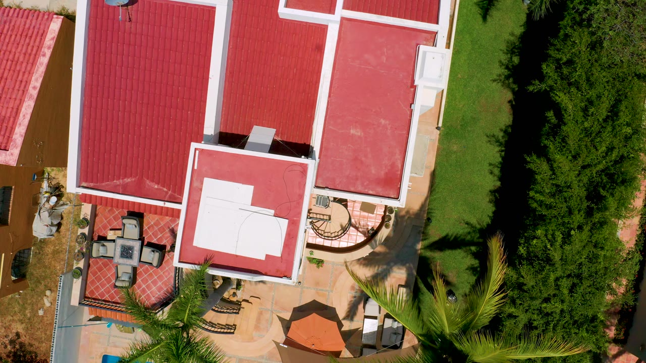 Closer overhead view of red roofs, white rooftop panel, patio seating, lawn, and hedges.