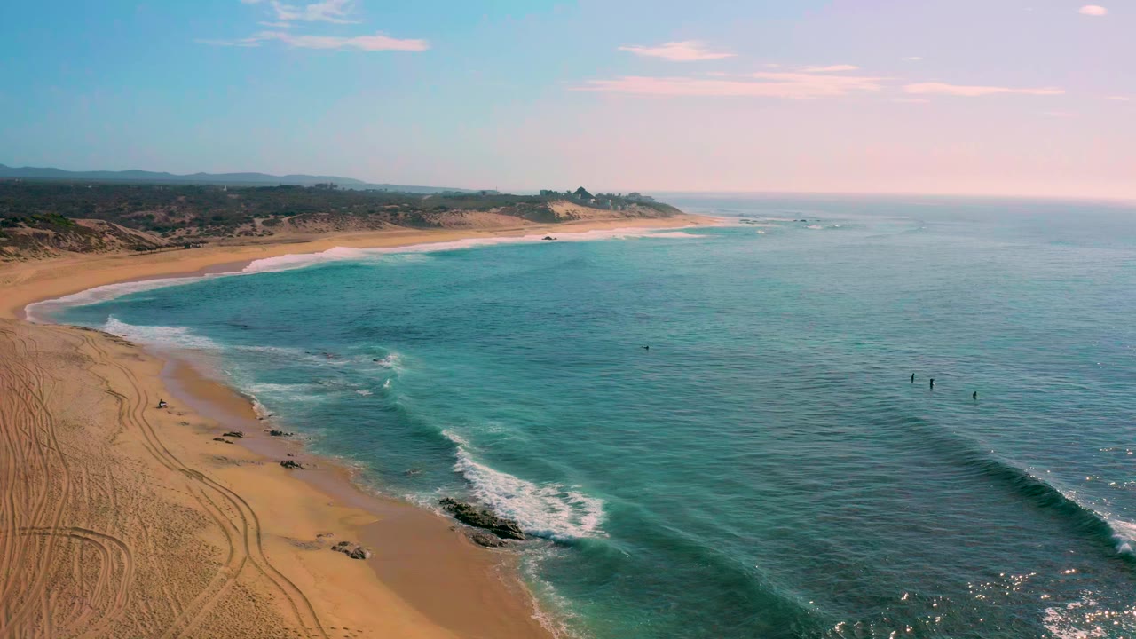 Aerial view of a sandy cove, turquoise water, and white surf.