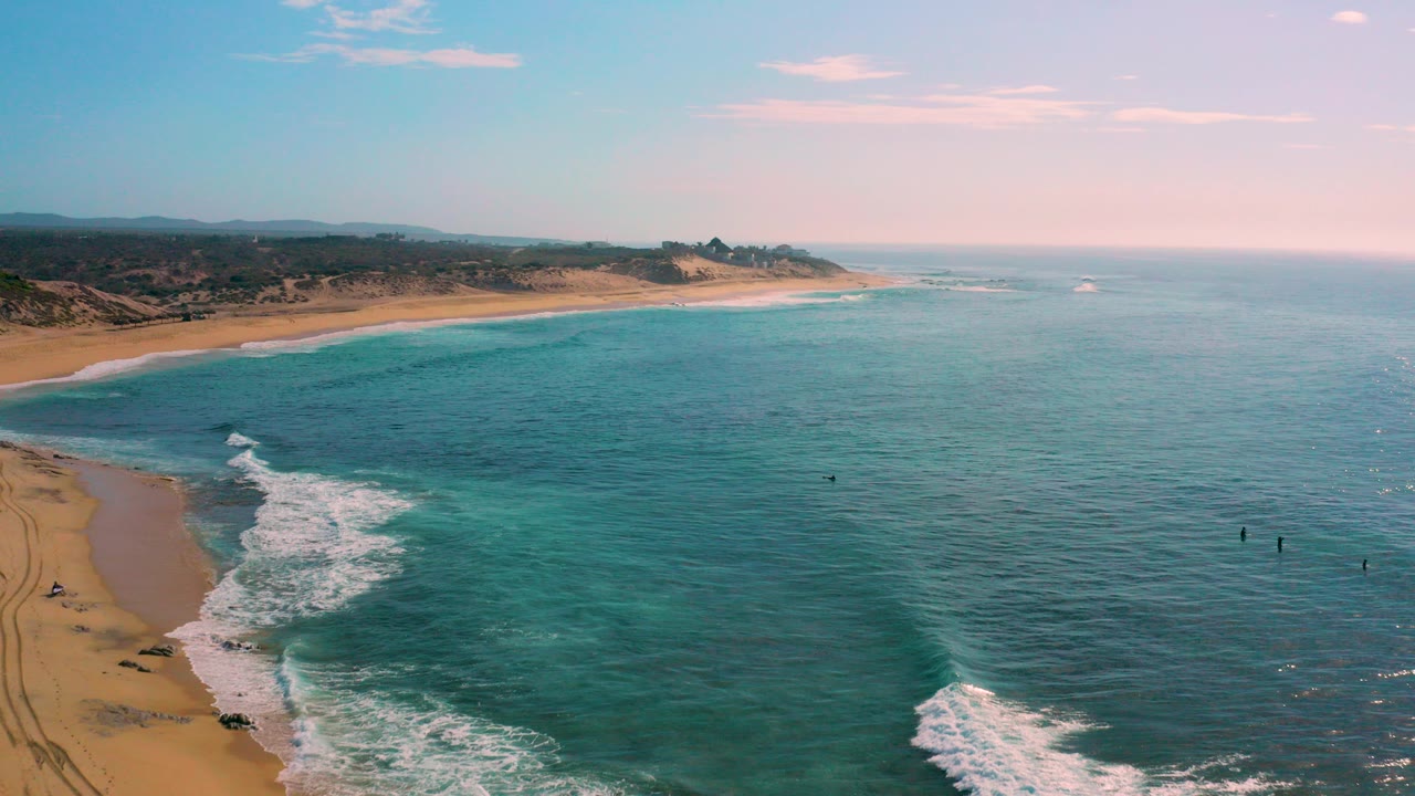 Aerial view of turquoise ocean and sandy beach with surf breaking along the shore.