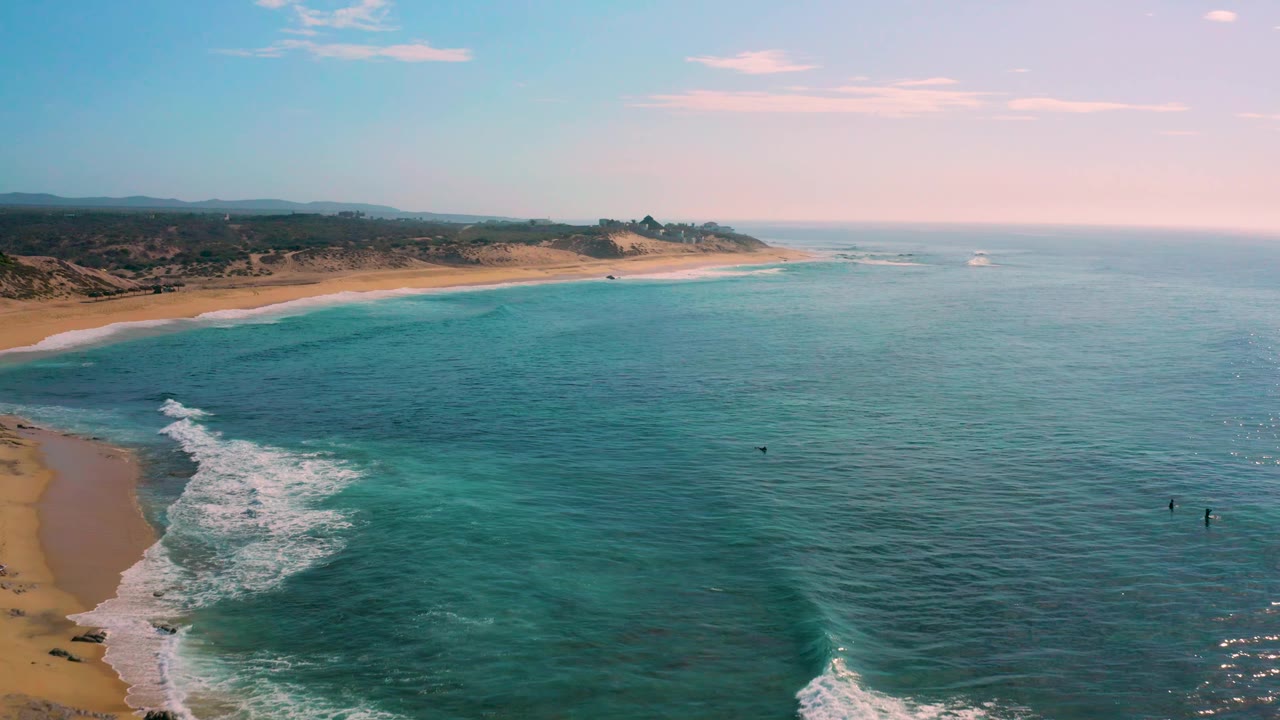 Aerial frame over Shipwrecks Beach in Baja California Sur, with the beach running across the upper left, darker reef-like patches under the water, small surf lines offshore, and no visible people.