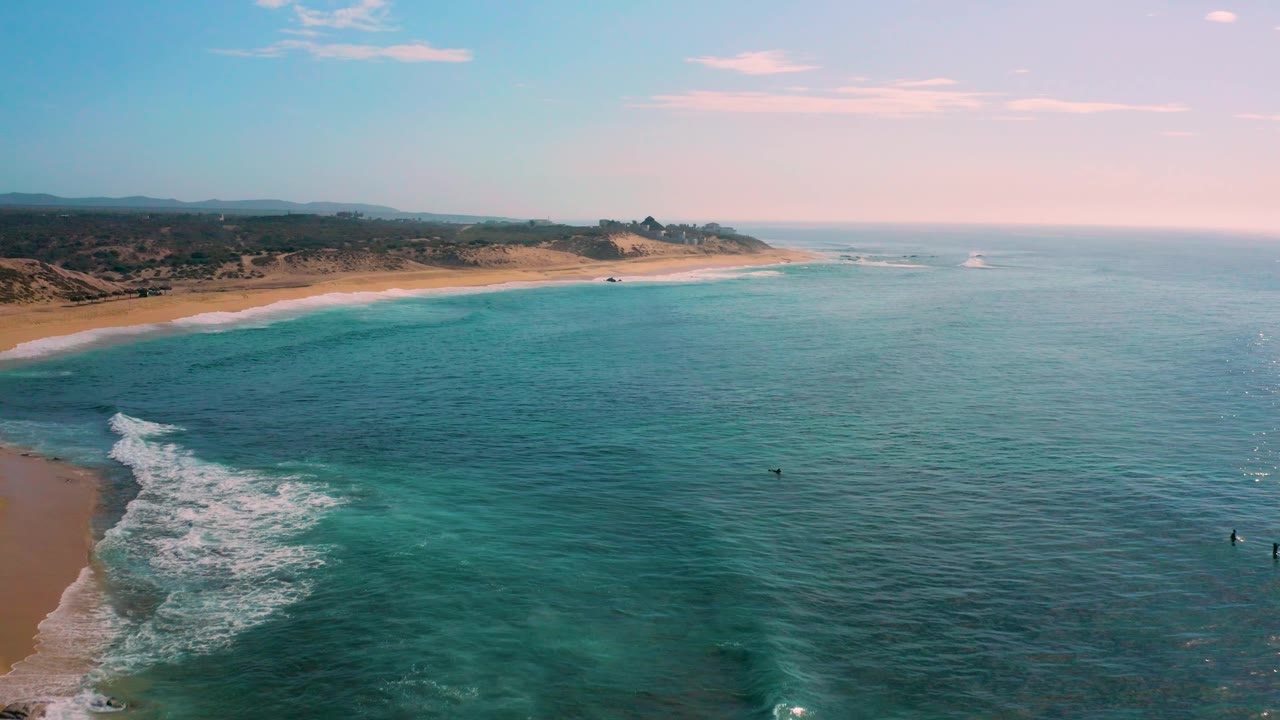 Aerial view of Shipwrecks Beach in Baja California Sur, where white surf curls into the lower left edge, turquoise water stretches across the frame, and no visible people appear on the sand or water.