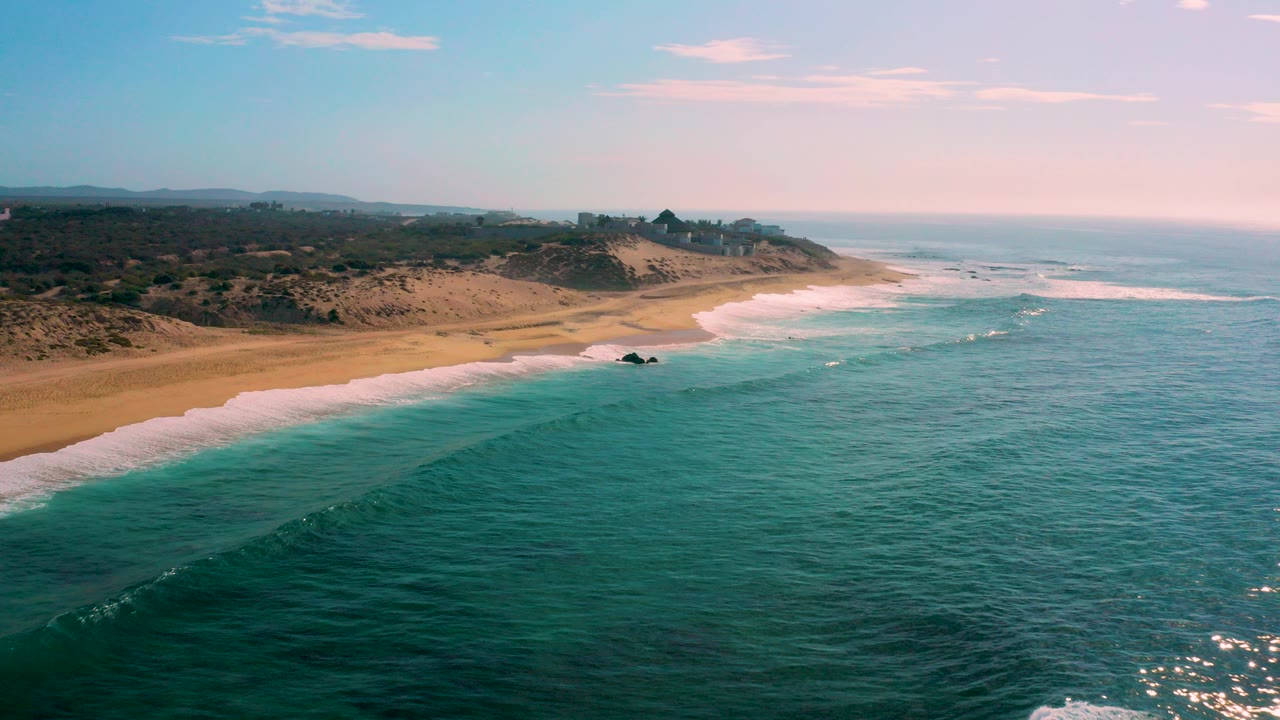 Aerial view of turquoise ocean beside a sandy beach and dunes.