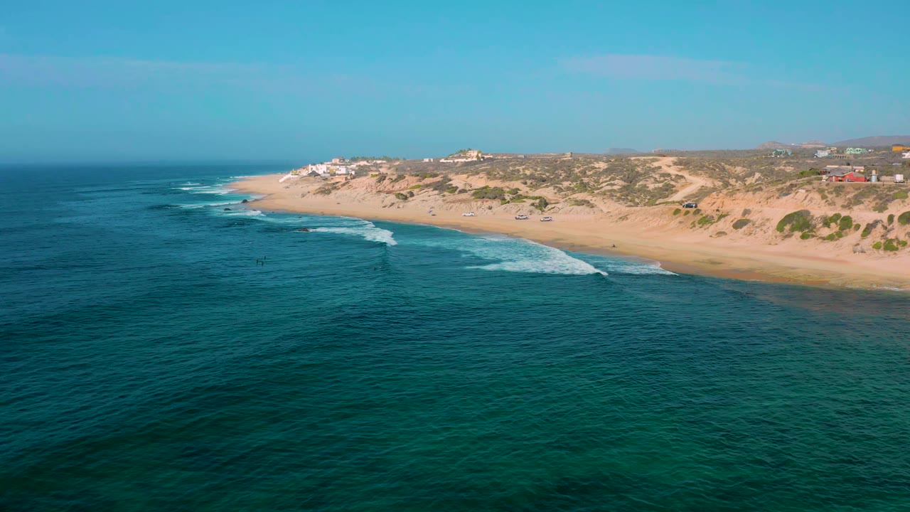 Wide drone view of waves breaking along a diagonal sandy shoreline.