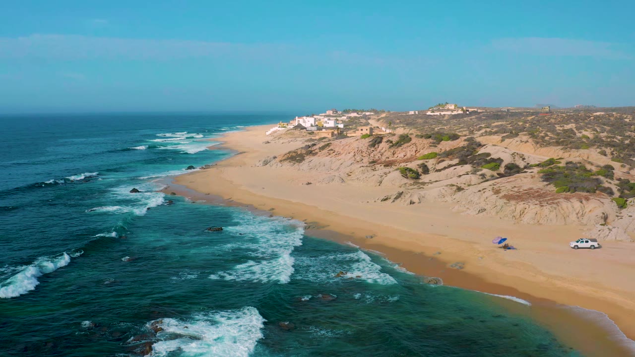 White waves break along a broad sandy shoreline below dunes.