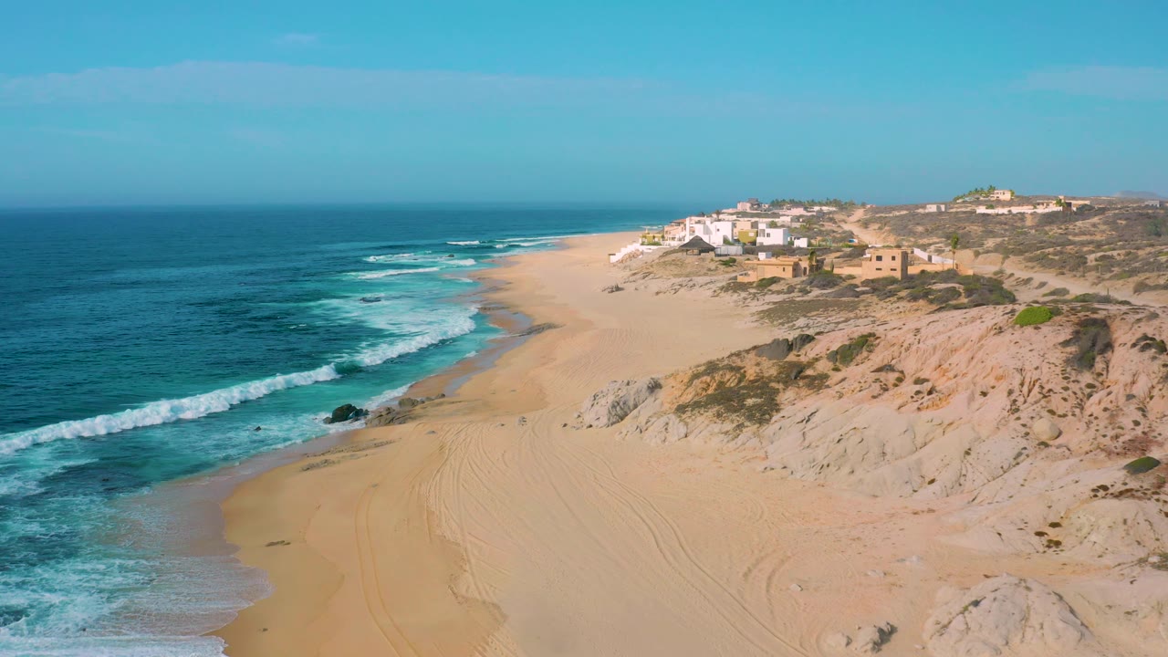 Surf rolls toward a sandy beach below dunes and a small coastal settlement.