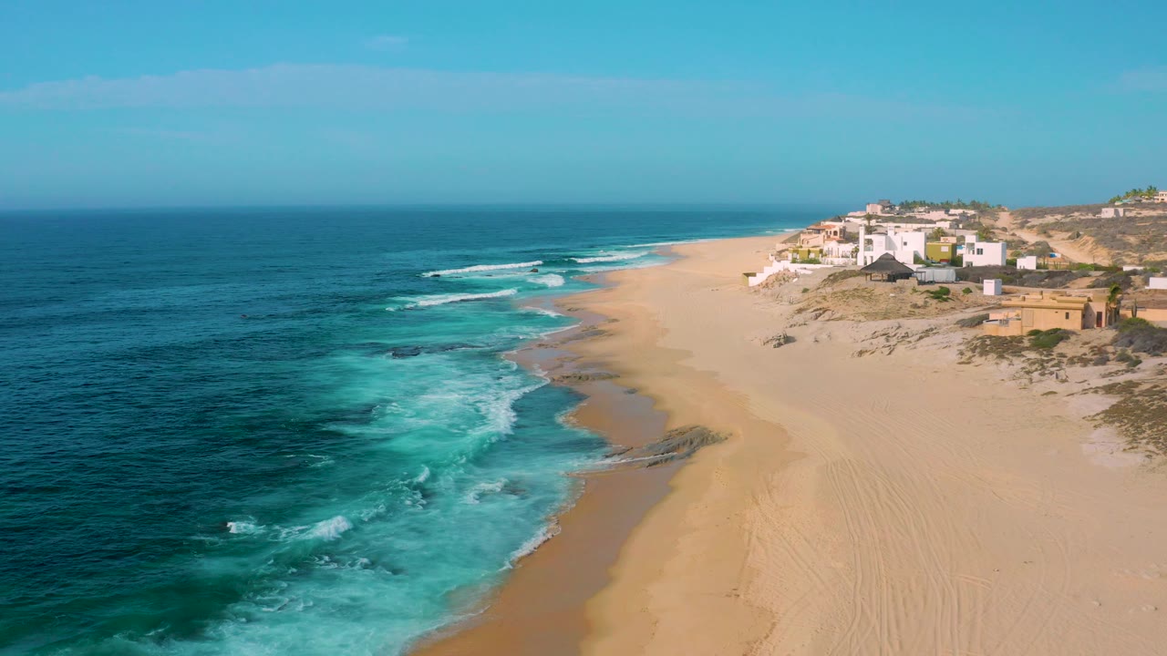 Wide beach and blue surf seen from above with houses at the far right.
