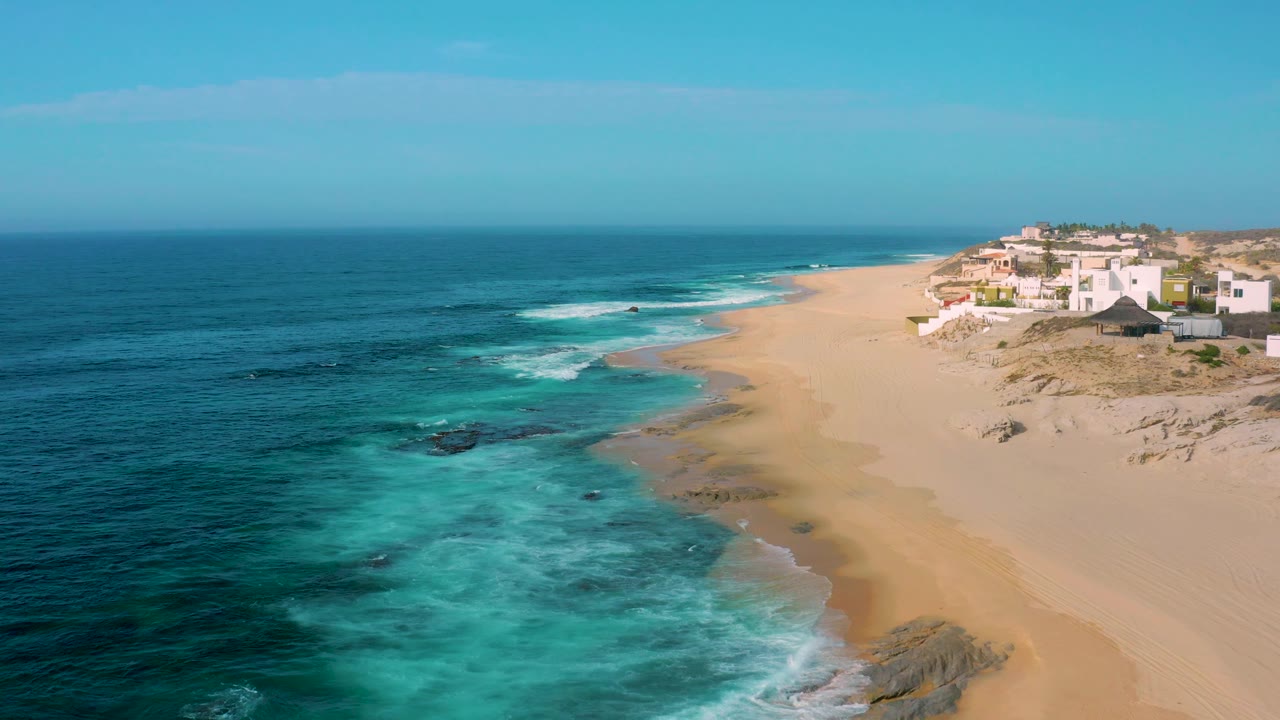 High aerial view of turquoise water, sand, and houses on dunes.
