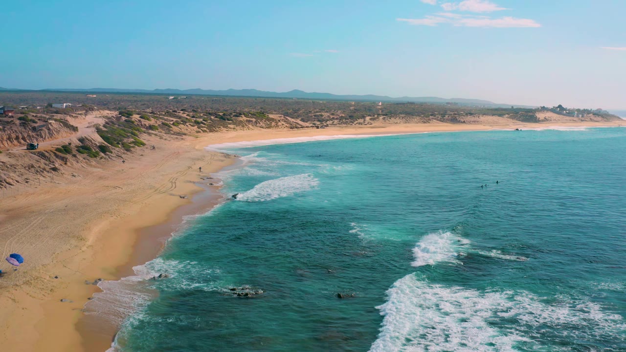 Wide aerial shoreline with surf curling along the sand.