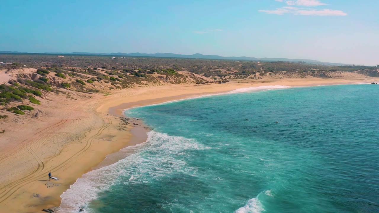 Wide aerial beach curve with green-blue water and low scrub inland.
