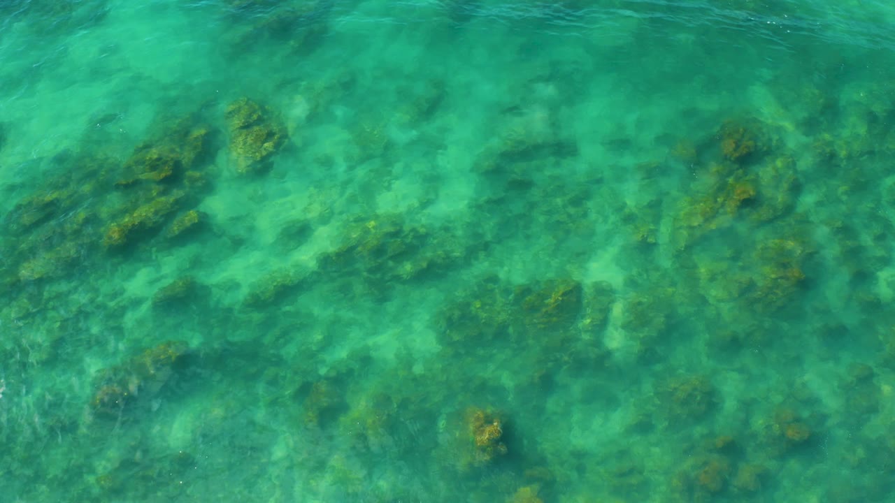 Top-down view of turquoise water and scattered submerged coral forms at Shipwrecks Beach, Baja California Sur, with no visible people.
