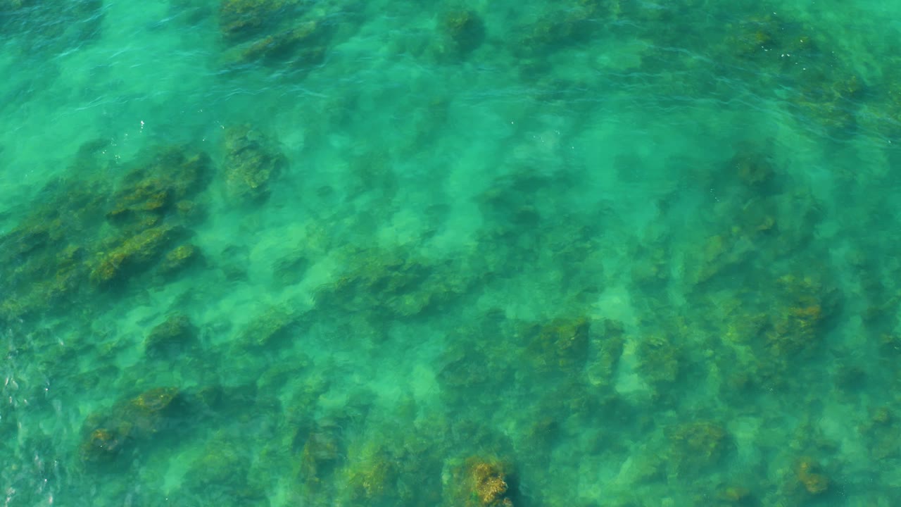 Overhead aerial view of green-blue ocean with darker reef bands below the surface at Shipwrecks Beach, and no visible people.