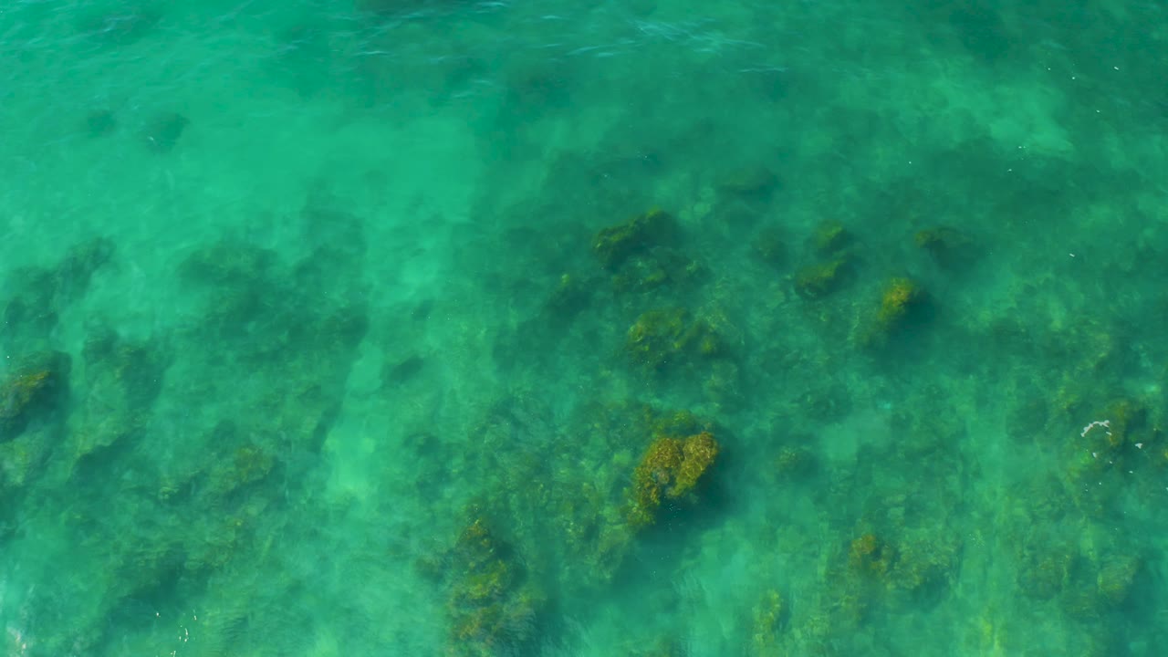 Turquoise overhead water at Shipwrecks Beach in Baja California Sur shows scattered dark rock and coral shapes spread across the sandy bottom, with no visible people.