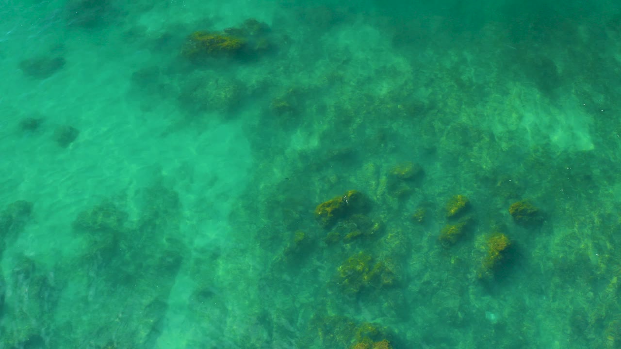 Overhead view of turquoise shallow water and dark submerged rocks at Shipwrecks Beach in Baja California Sur, with no visible people.
