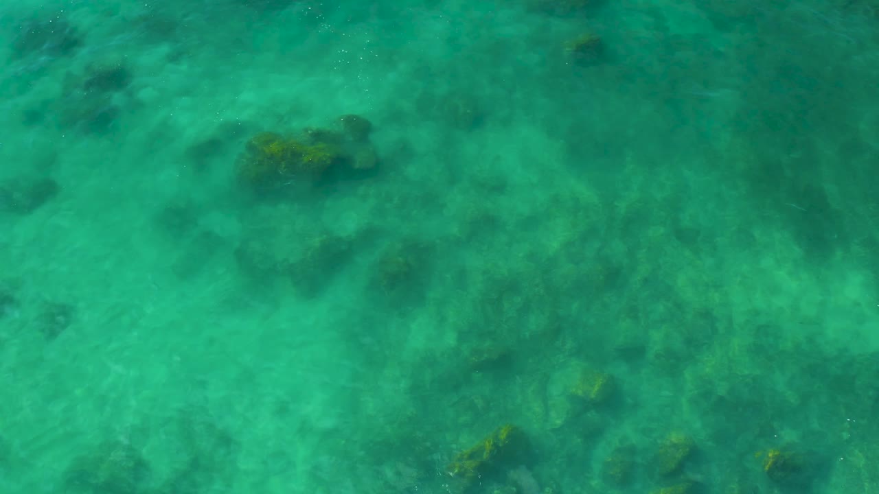 Clear water shifts across darker submerged rocks and pale sand at Shipwrecks Beach, Baja California Sur, with no visible people.