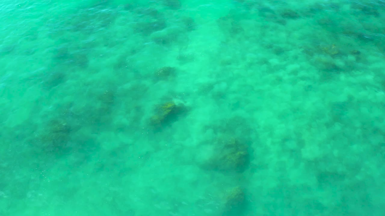 Overhead turquoise sea surface with dark submerged patches.