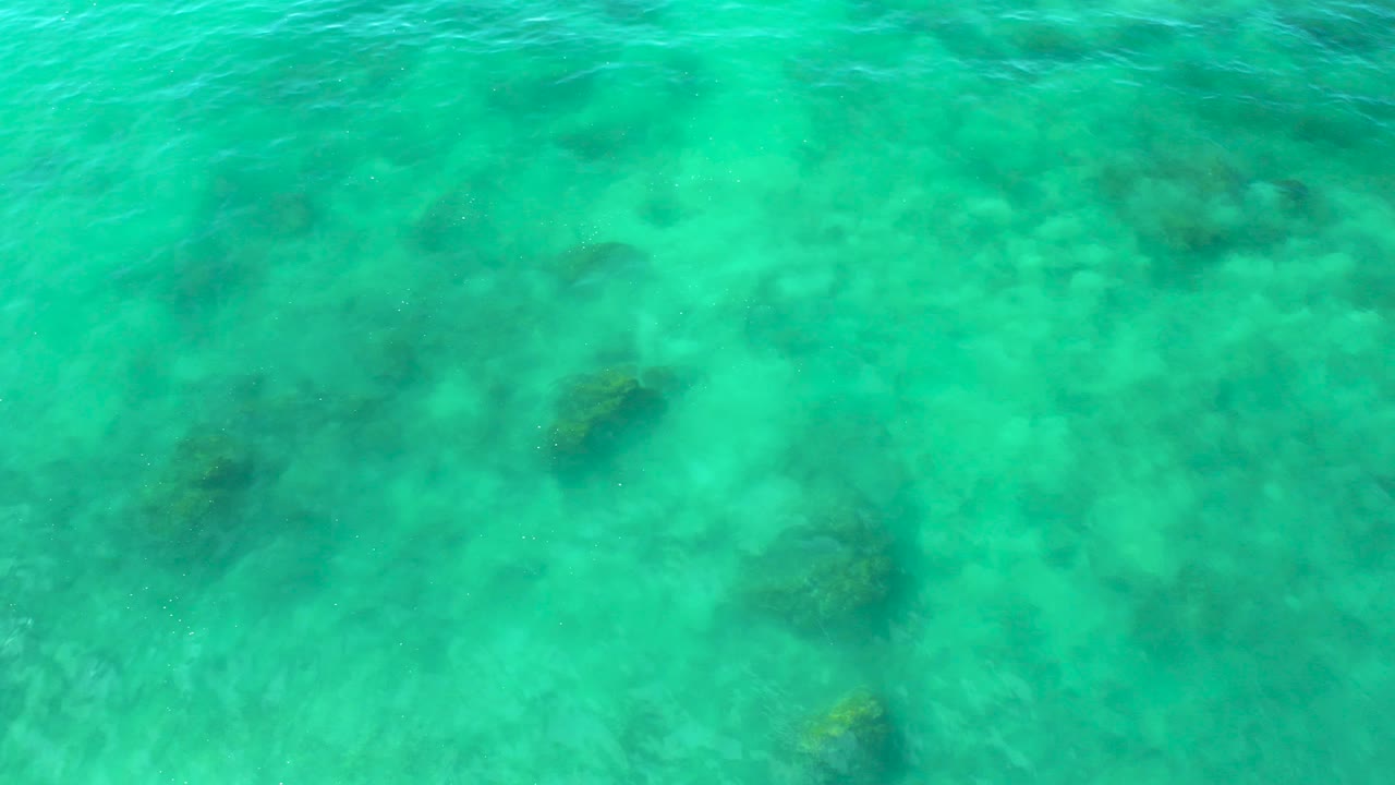 Top-down view of turquoise sea at Shipwrecks Beach, showing a brighter ripple band over shallow bottom texture with no visible people.