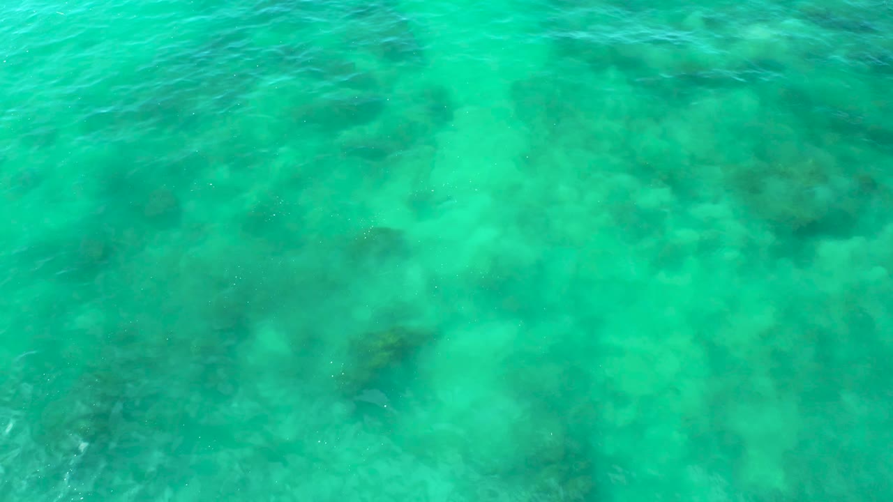 Clear green-blue ocean water at Shipwrecks Beach, Baja California Sur, shows mottled pale seabed and darker underwater areas with no visible people.