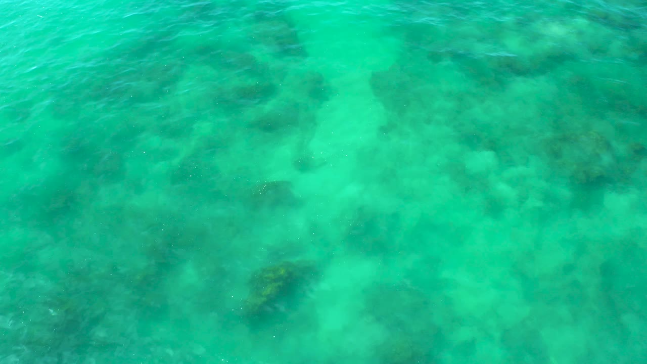 Sunlit turquoise water at Shipwrecks Beach, Baja California Sur, carries faint ripples over darker submerged shapes, with no visible people or structures.