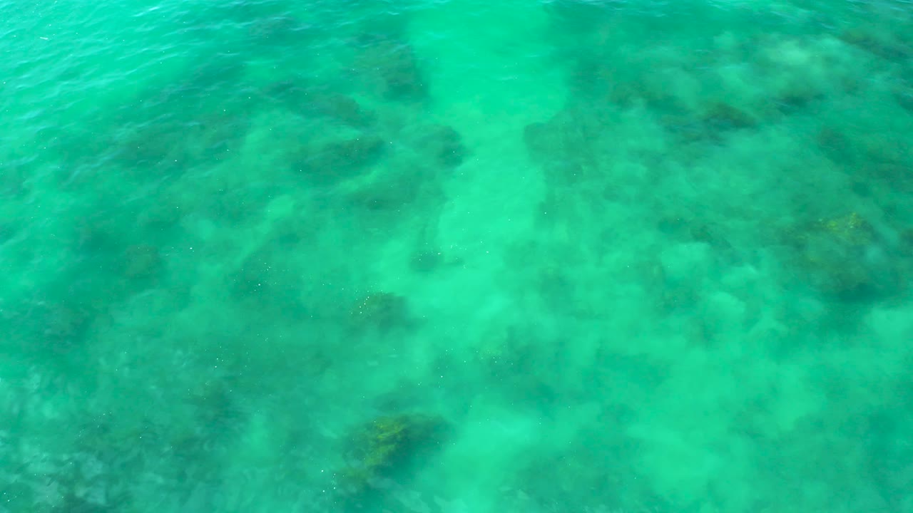 Aerial-looking view of shallow turquoise sea at Shipwrecks Beach, Baja California Sur, with soft wave texture across the upper water and no visible people.