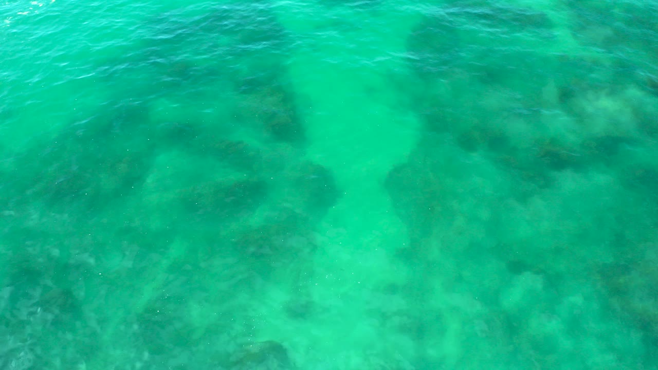 Overhead view of turquoise water at Shipwrecks Beach, Baja California Sur, with dark submerged rock shapes beneath the surface and no visible people.