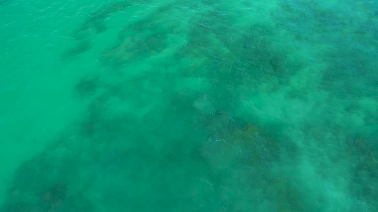 Green ocean surface at Shipwrecks Beach, Baja California Sur, with soft wave streaks crossing darker reef-like patches below and no visible people.
