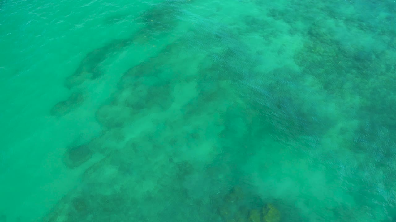 Top-down Shipwrecks Beach sea surface with faint diagonal wave lines crossing turquoise water above dark underwater formations, with no visible people.