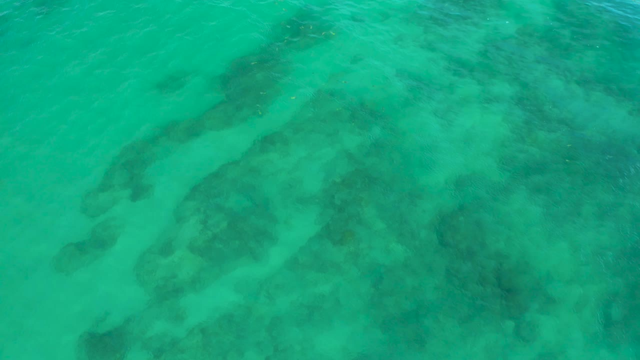 A straight-down aerial frame over Shipwrecks Beach water shows darker underwater formations separated by pale sandy streaks, with no visible people.