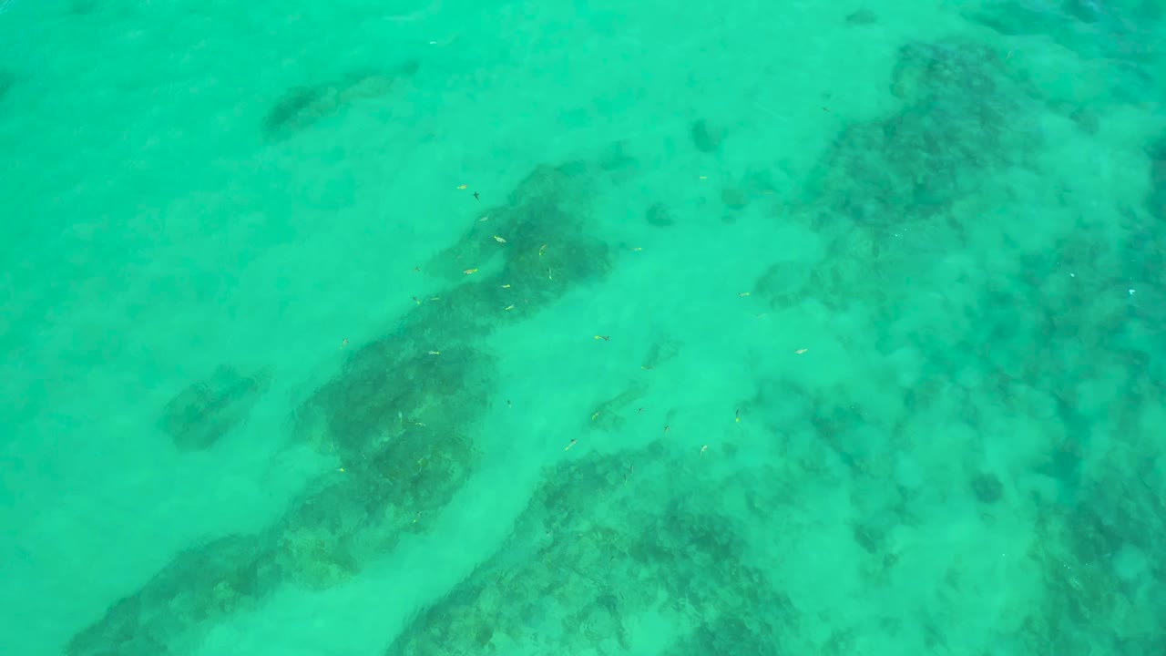 Clear green-blue water fills the frame at Shipwrecks Beach, Baja California Sur, with a broad dark patch near the lower left and no visible people.