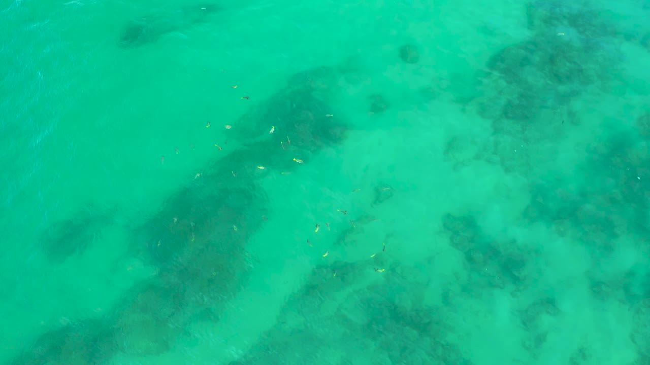 Turquoise shallow water fills the frame at Shipwrecks Beach, with uneven darker reef or rock shapes below the surface and no visible people.