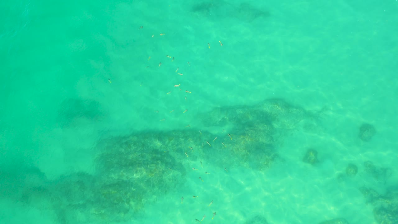 Top-down view of turquoise water at Shipwrecks Beach, Baja California Sur, with dark submerged reef or wreck-like shapes near the lower edge and no visible people.