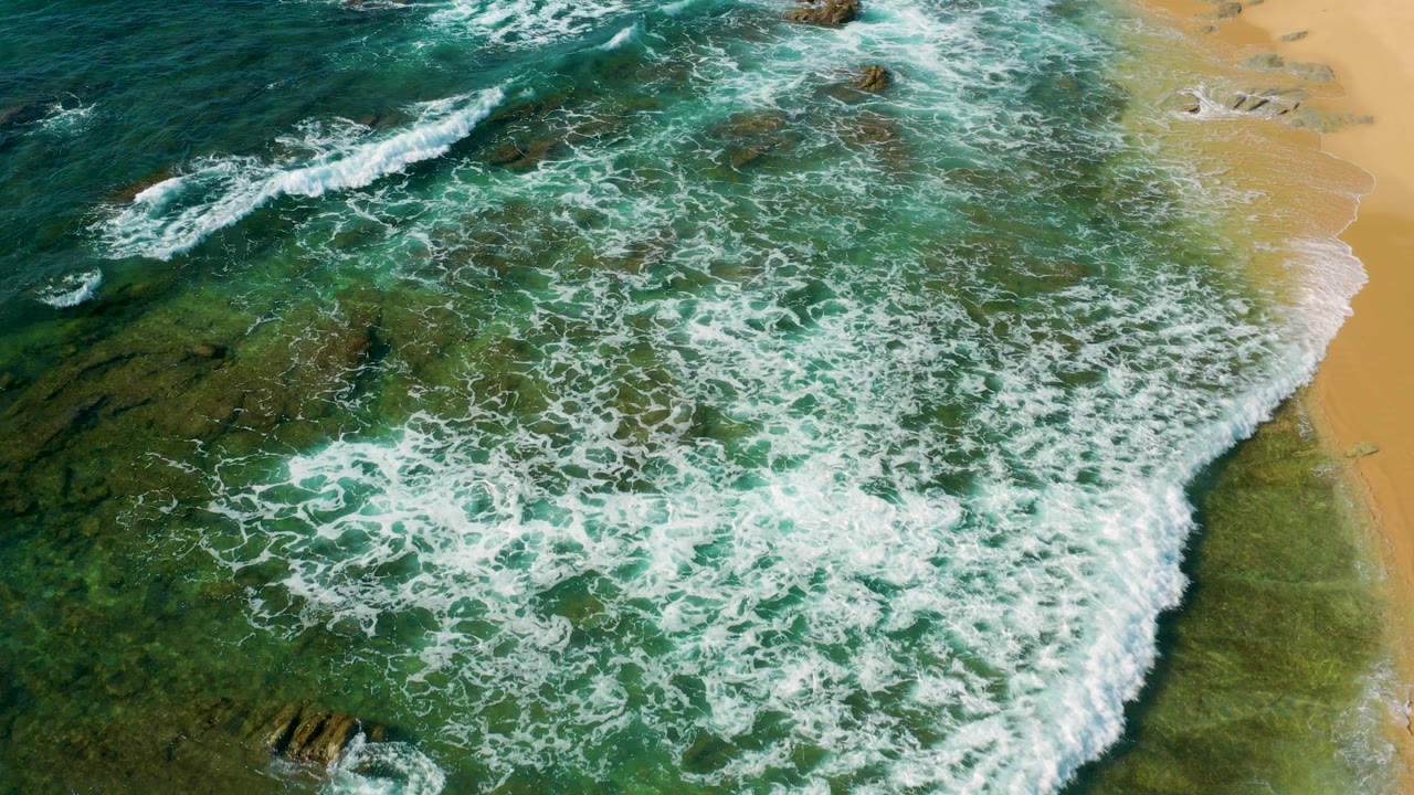 Overhead surf washing over rocks beside a sandy beach
