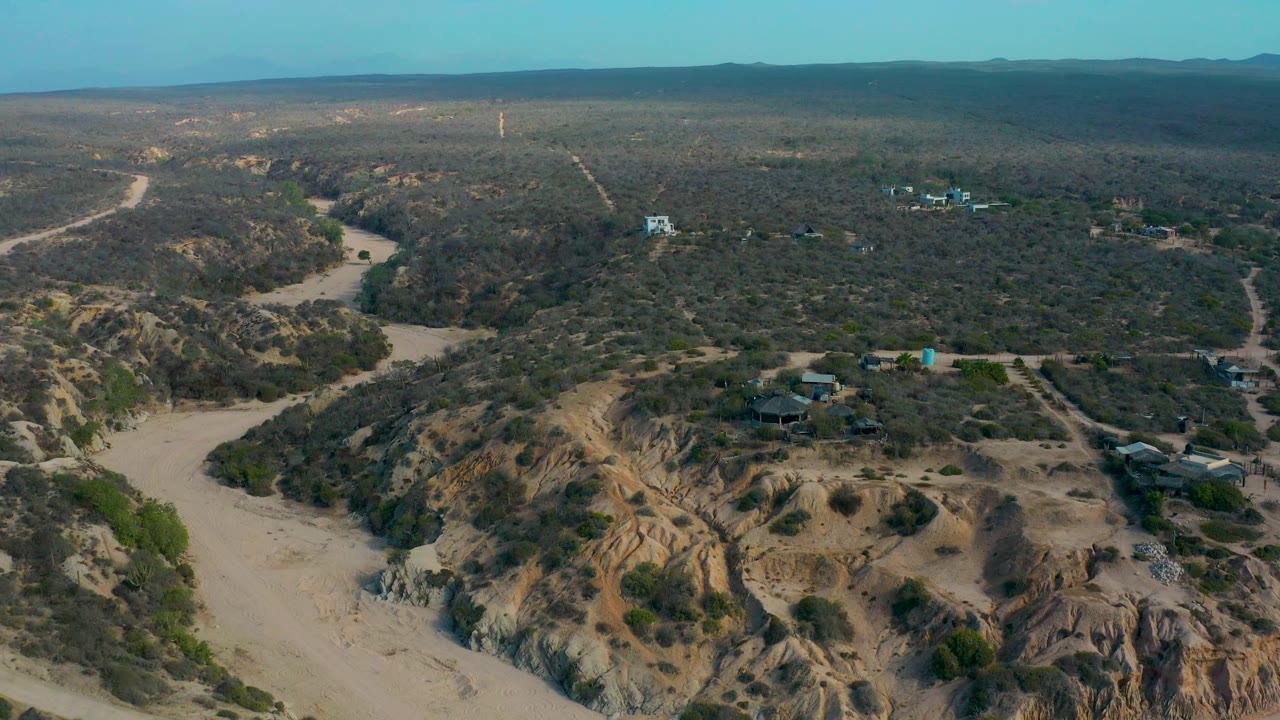 Aerial view across scrubby desert terrain, sandy wash, and scattered structures.