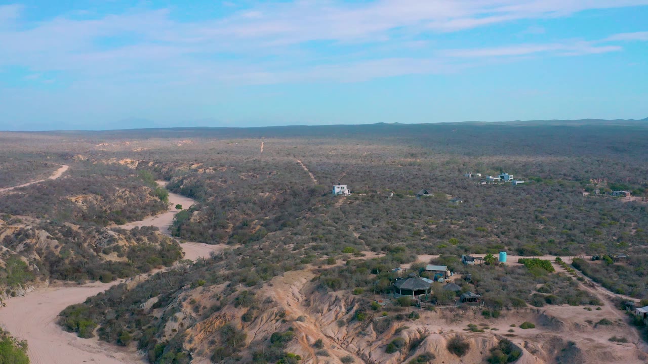 Aerial landscape with sandy wash, dune cuts, low shrubs, and scattered structures.