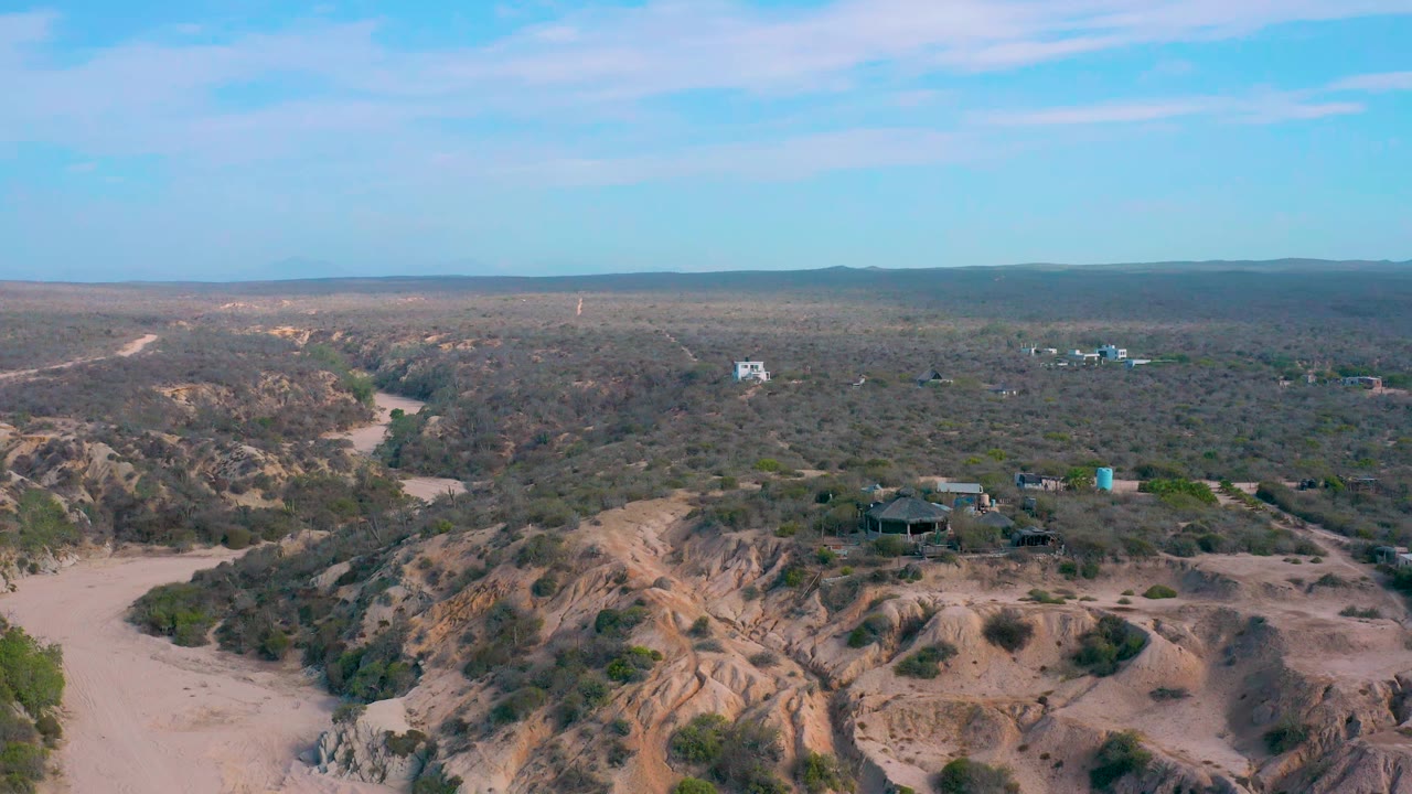 Elevated view of tan ridges, sandy wash, scrubland, and distant buildings.