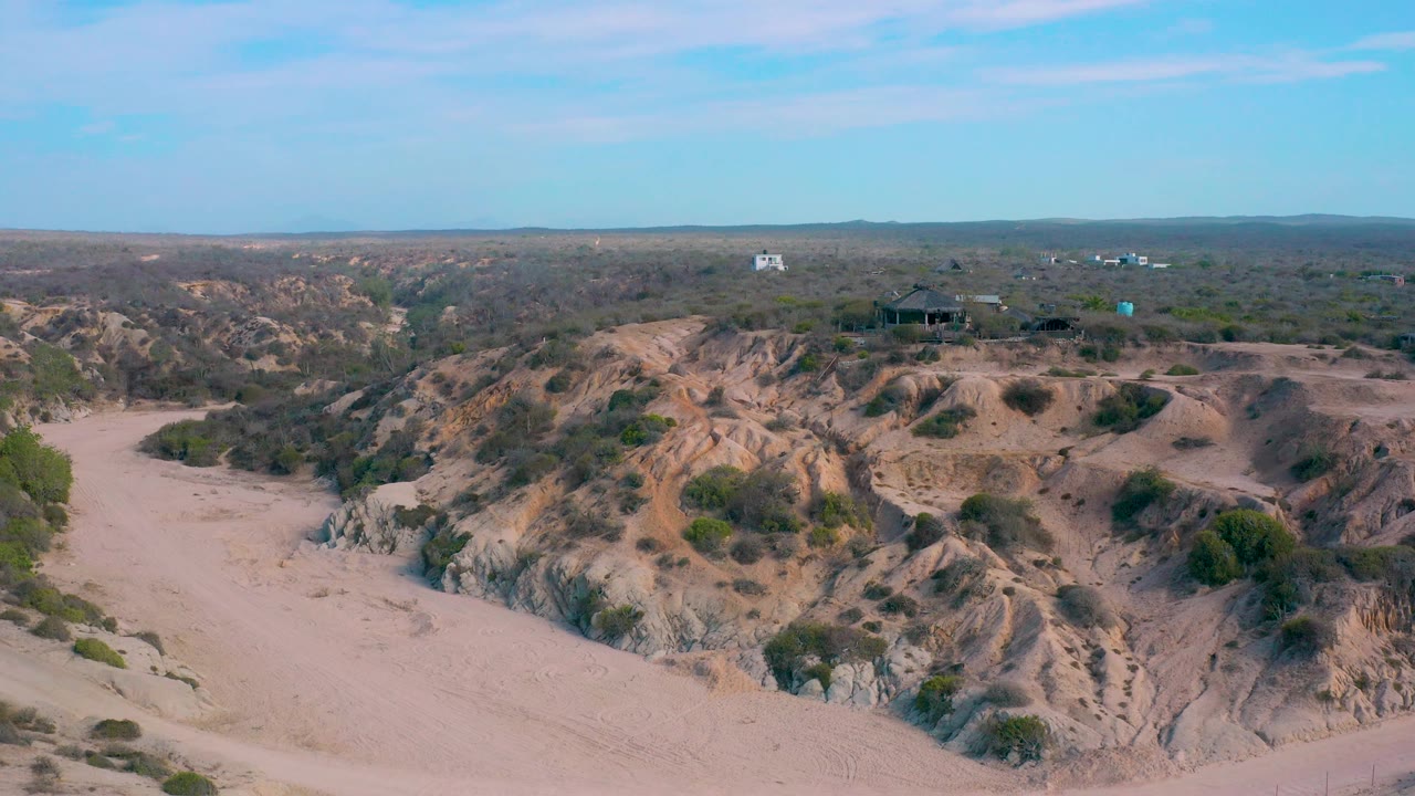 Broad desert aerial with sand, shrubs, ridges, and distant horizon.