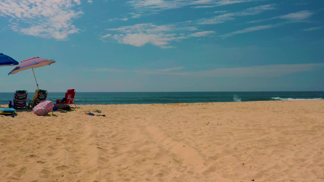 At Shipwrecks Beach in Baja California Sur, beach chairs and umbrellas sit at the far left edge of a wide sandy shoreline with ocean and sky behind them.
