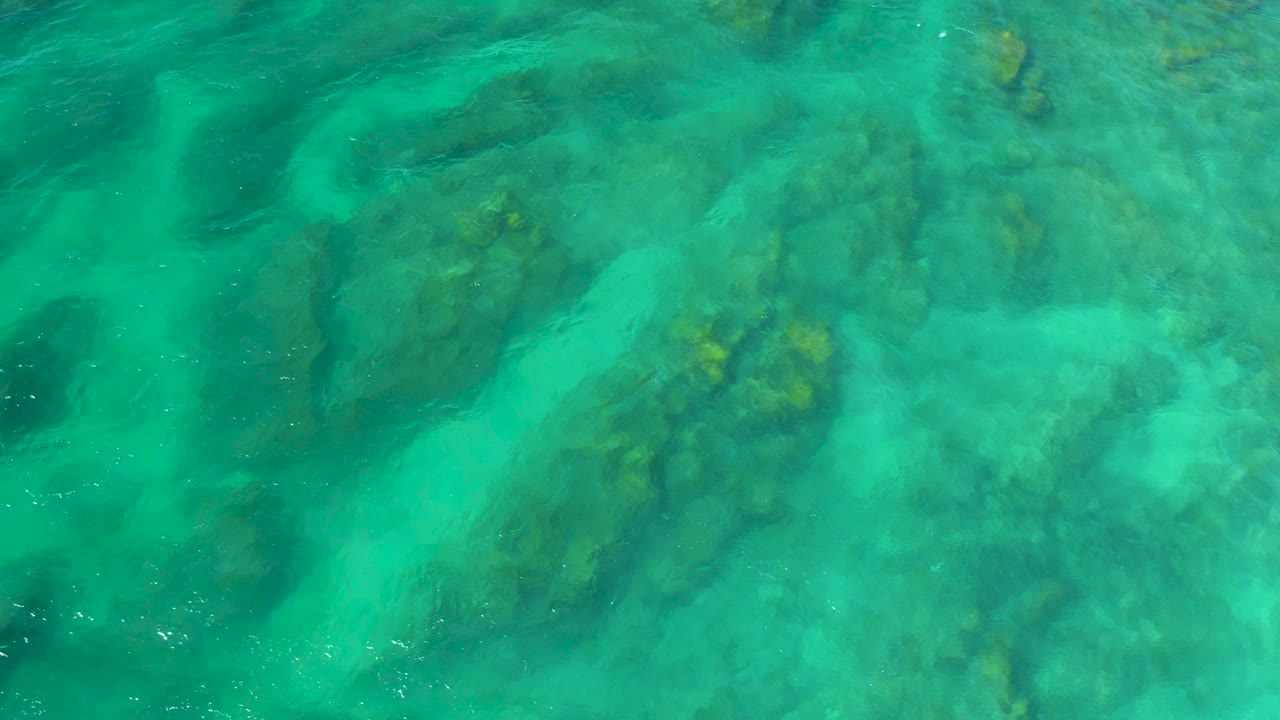Overhead view of turquoise water above submerged reef patches at Shipwrecks Beach, Baja California Sur, with pale sand channels and no visible people.