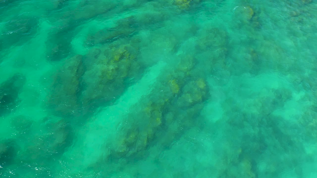 Bright turquoise surface water shows clustered submerged reef patches and soft sandy gaps at Shipwrecks Beach, Baja California Sur, with no visible people.