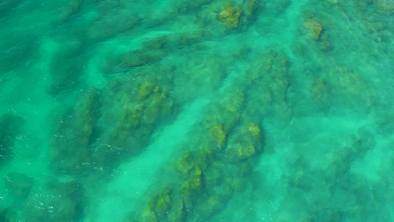 Straight-down aerial view at Shipwrecks Beach, Baja California Sur, with bright turquoise water, clustered submerged rocks, and no visible people.