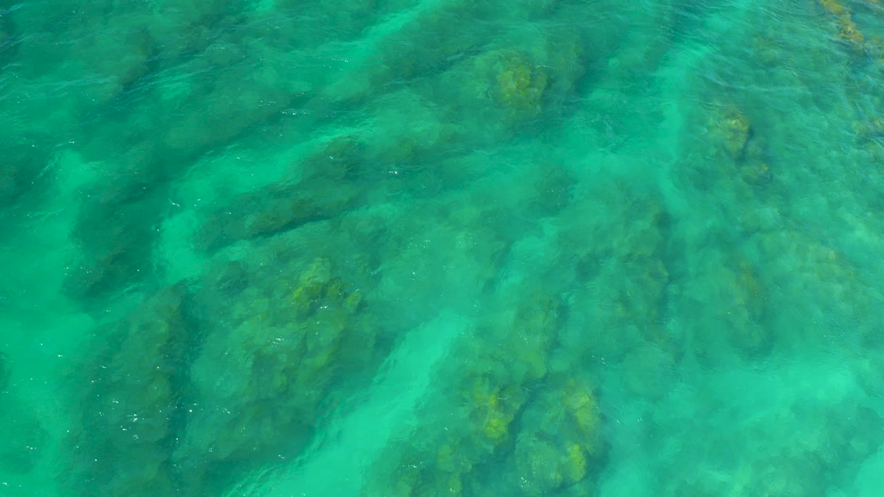 Overhead view of turquoise water flowing across submerged rocks at Shipwrecks Beach, Baja California Sur, with no visible people.