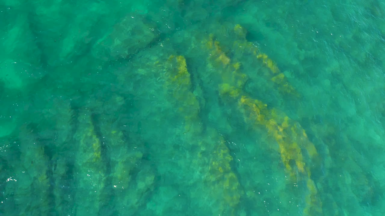 Clear green-blue water with diagonal underwater rocks.