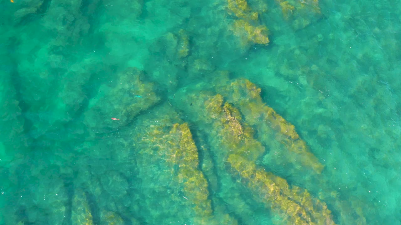 Overhead blue-green water reveals a rocky seabed near Shipwrecks Beach in Baja California Sur, Mexico, with no visible people or vessels.