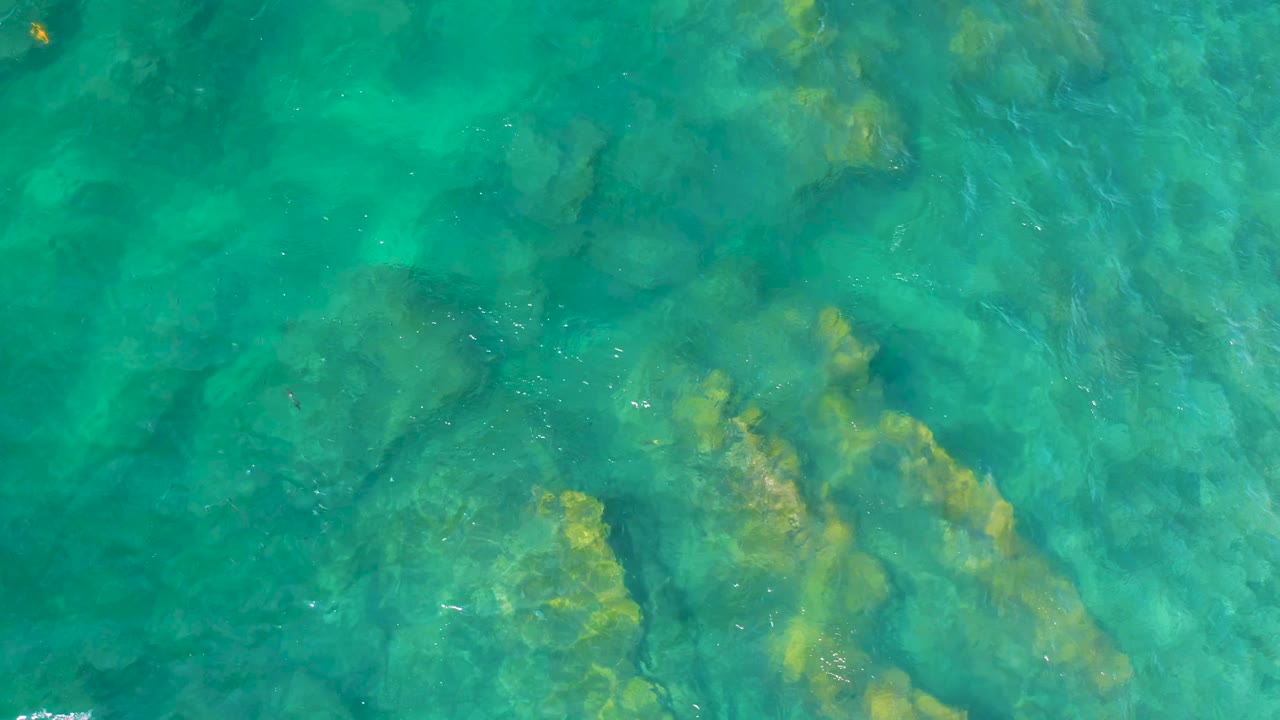 Clear teal water covers uneven submerged rock shelves at Shipwrecks Beach, Baja California Sur, with faint ripples and no visible people.