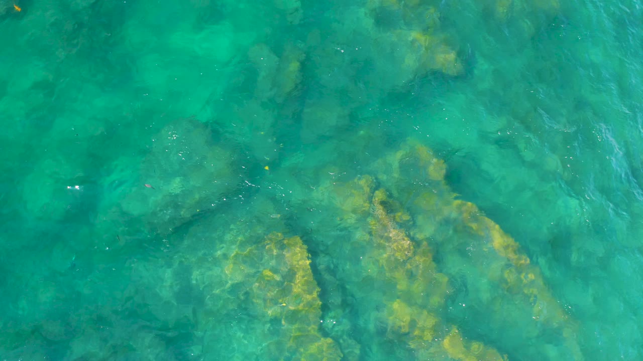 Aerial view of green-blue ocean water with broad submerged rocks beneath the surface at Shipwrecks Beach, Baja California Sur, and no visible people.
