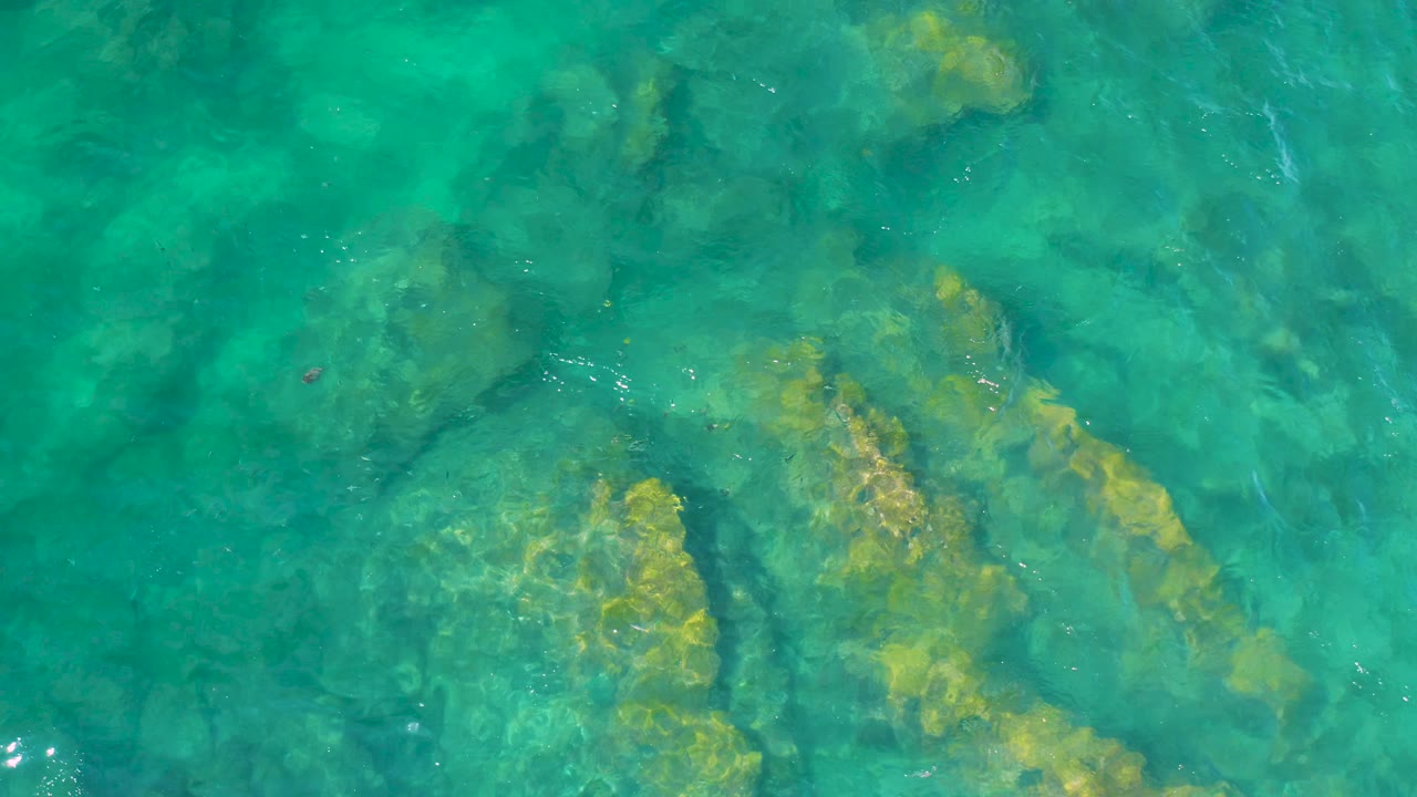 Turquoise ocean water reveals darker channels between submerged rocks at Shipwrecks Beach, Baja California Sur, with no visible people.