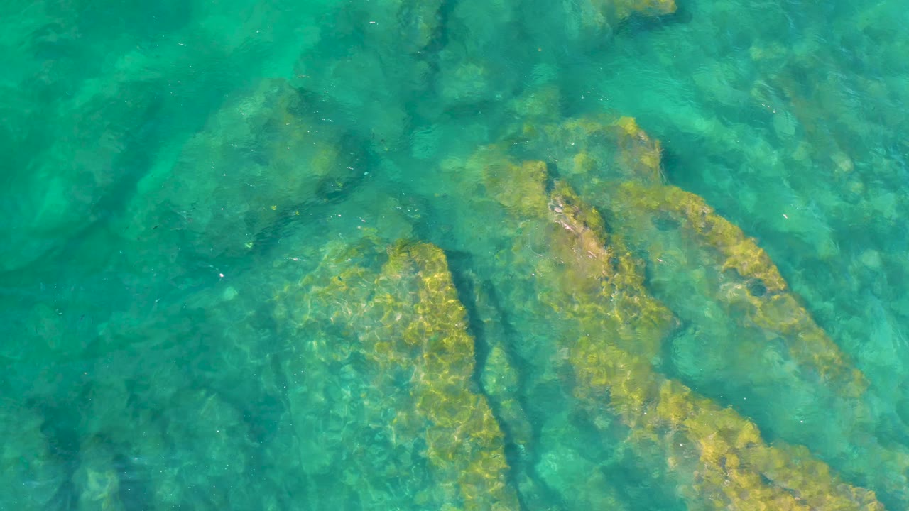 Long submerged rocks sit diagonally beneath blue-green ocean water at Shipwrecks Beach, Baja California Sur, with no visible people.