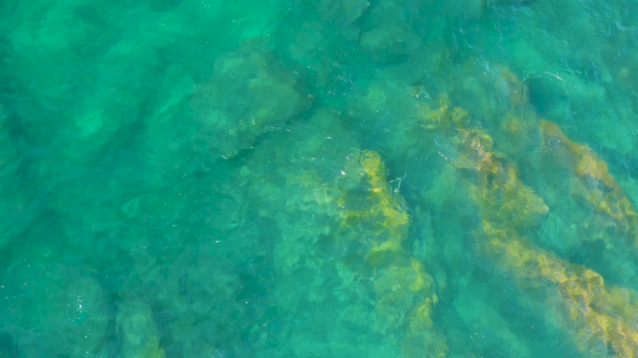 Green-blue ocean surface at Shipwrecks Beach with broad submerged rock shapes visible under rippled water and no visible people.