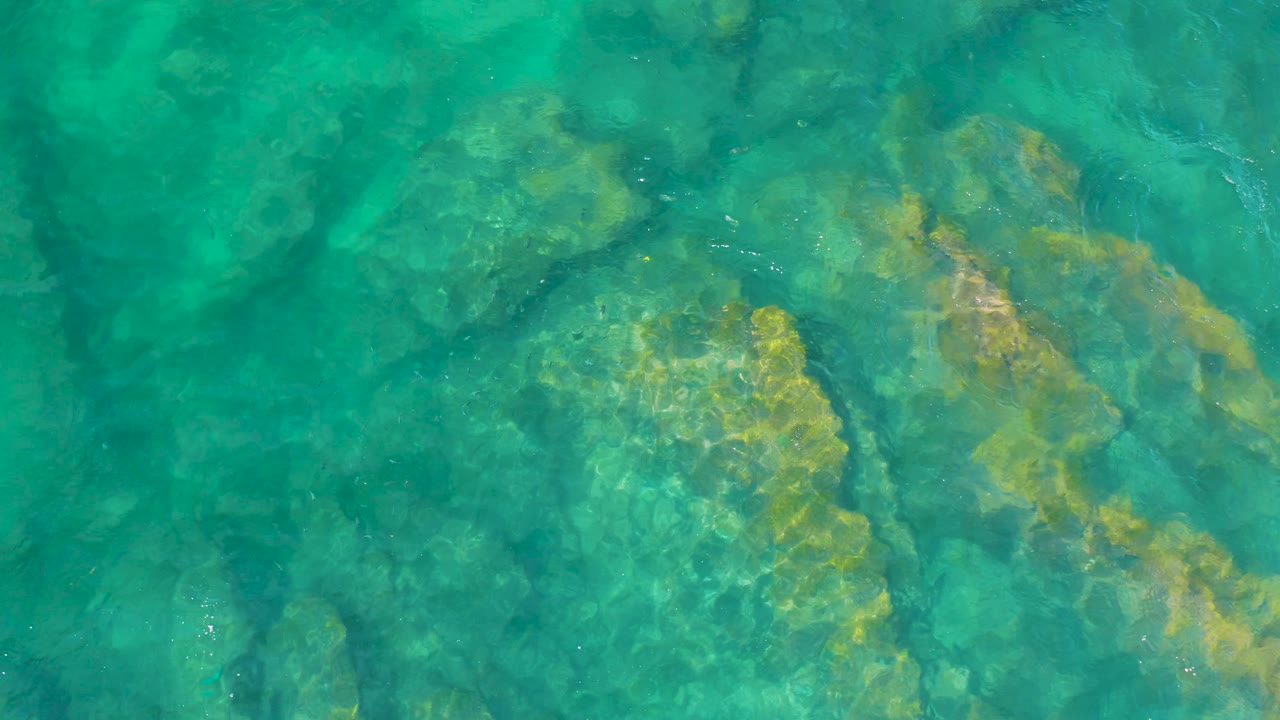 Teal ocean water fills the frame at Shipwrecks Beach, with larger submerged rocks clustered toward the lower right and no visible people.